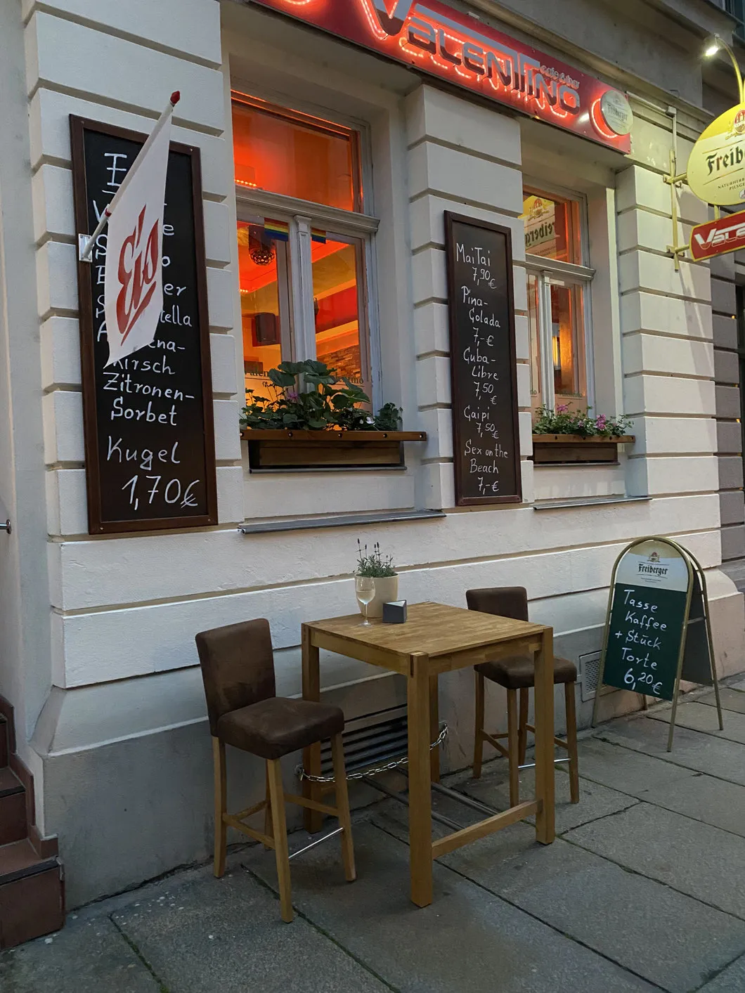 Fassade des Valentino in der Jordanstraße mit roter Leuchtschrift, Kreidetafeln und Stehtisch